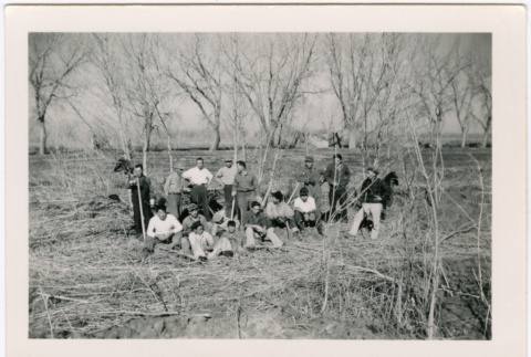 Group of men sitting near bare trees with barracks in background (ddr-densho-329-1376)
