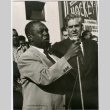 Two men speaking at a microphone by crowd (ddr-densho-426-982)