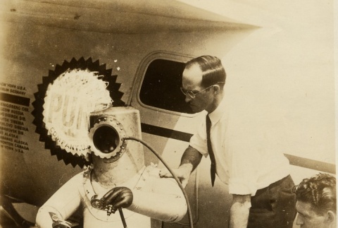 Wiley Post sitting in front of his plane in a pressurized suit (ddr-njpa-1-1323)