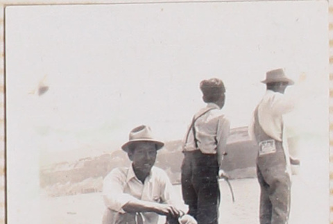 Three men standing on log along shore, one facing camera (ddr-densho-464-86)