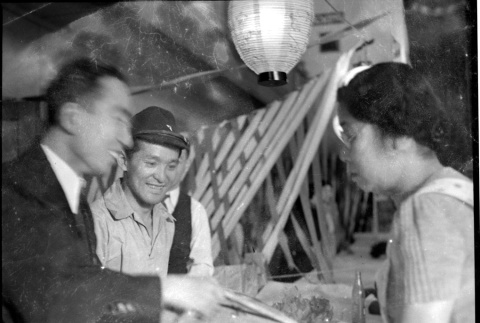 Two men with large bundle wrapped in rope, talking to woman (ddr-densho-426-1762)
