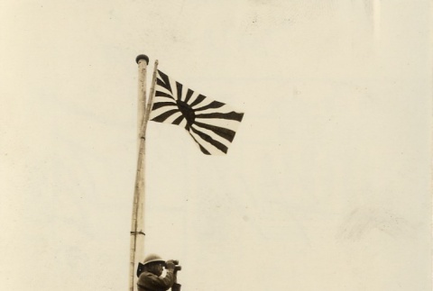 A soldier looking through binoculars under a Japanese flag (ddr-njpa-6-43)