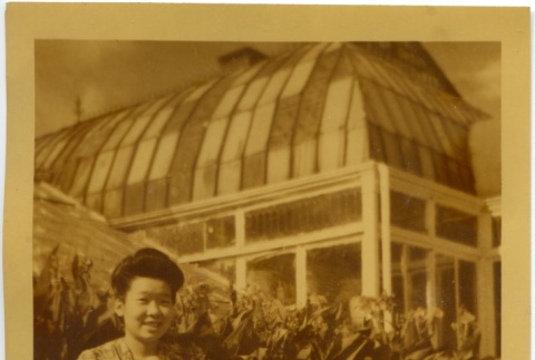 Miyo Kusunoki sitting in front of a greenhouse (ddr-manz-6-107)