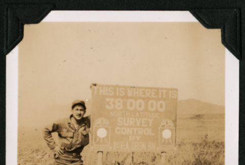 Walter Matsuoka poses by a sign at the 38th parallel north (ddr-densho-390-92)