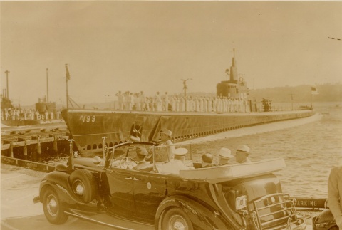 Franklin D. Roosevelt riding in a car with an naval submarine in the background (ddr-njpa-1-1498)