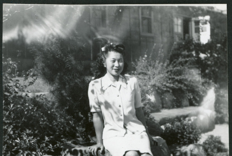 Photograph of a woman sitting on a rock in front of the Manzanar hospital (ddr-csujad-47-256)