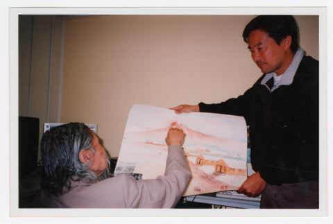 Narrator pointing at Heart Mountain painting Tom Ikeda is holding (ddr-densho-506-34)
