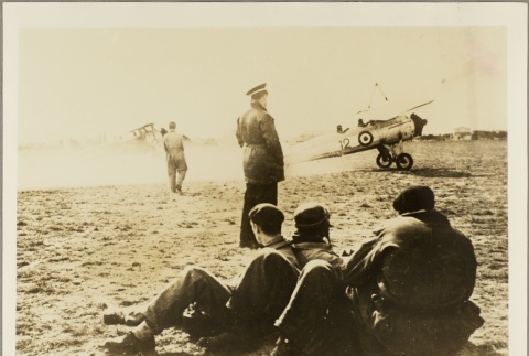 Men sitting on an airfield watching a plane prepare to take off (ddr-njpa-13-1336)
