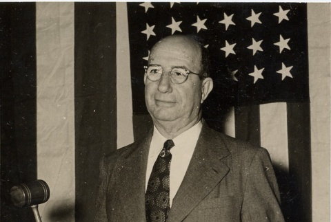 Judge posing in front of a flag, holding a gavel (ddr-njpa-2-792)