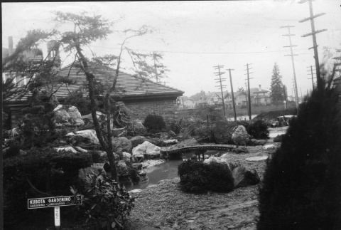 Bridge in a garden with a Kubota Gardening Company sign (ddr-densho-354-117)