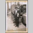 Man with glasses carrying a bag standing by row of cars (ddr-densho-483-992)