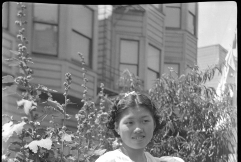 Girl holding kitten standing by hollyhocks (ddr-densho-426-2017)