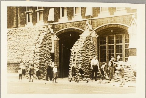 Men stacking sandbags against a building while young boys watch (ddr-njpa-13-276)