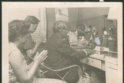 Man sitting at desk, with two women behind him (ddr-densho-293-196)