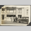Group around a car in front of building 