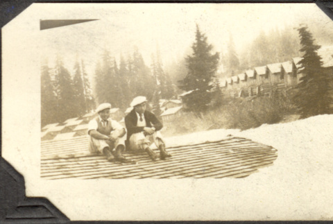 Two men sitting by row of cabins in the snow (ddr-densho-326-481)