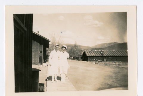 Two nurses standing on wooden walkway outside of barracks (ddr-densho-223-38)