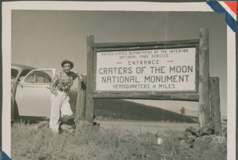 Man standing next to the Craters of the Moon National Monument sign (ddr-densho-201-949)