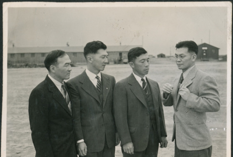 Four men in suits with barracks in background (ddr-densho-523-141)