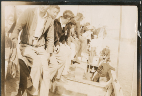 Group of men sitting on dock next to boat (ddr-densho-483-567)