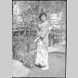 Tomoye (Nozawa) Takahashi in kimono standing by flowering trees (ddr-densho-426-2047)