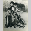 Photograph of three boys, two are on a tricycle, the other is holding a stick (ddr-csujad-47-50)
