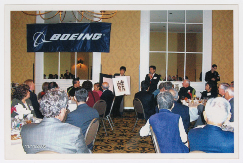 Tom Ikeda speaking at Inouye and Nisei vets luncheon with caligraphy art piece (ddr-densho-506-150)