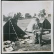 Man kneeling next to tent with gear (ddr-densho-434-465)
