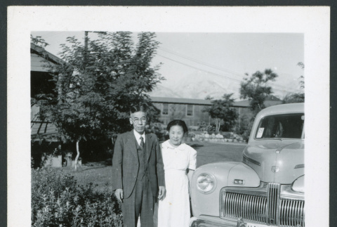 Photograph of a couple posing in front of a car near the Manzanar hospital (ddr-csujad-47-258)