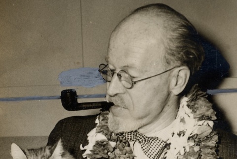 A man wearing leis, holding a cat and smoking a pipe (ddr-njpa-1-2470)