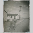 Two men walking on road by barracks (ddr-densho-493-105)