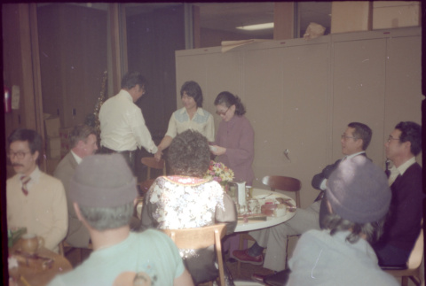 Tomoye Takahashi standing in front of group seated at tables (ddr-densho-426-612)
