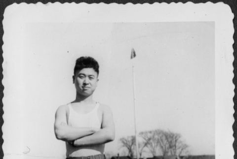Man standing in field, flag pole in background (ddr-densho-434-401)