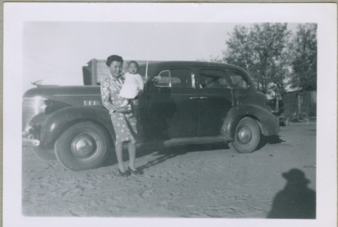 A woman holding a baby in front of a car (ddr-densho-300-38)