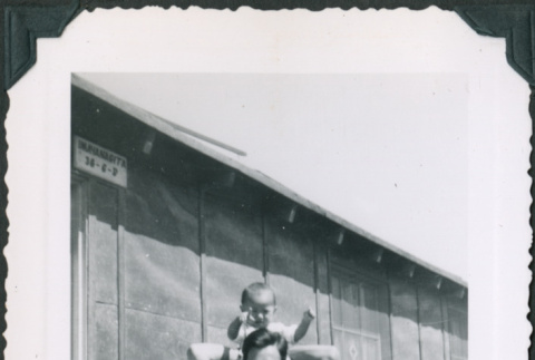 Man with baby on his shoulders outside barracks (ddr-densho-483-1095)