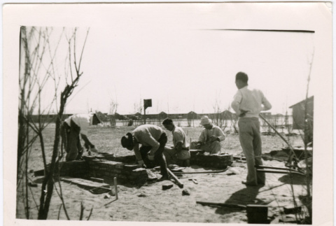 Five men building with bricks with barracks in background (ddr-densho-329-1374)