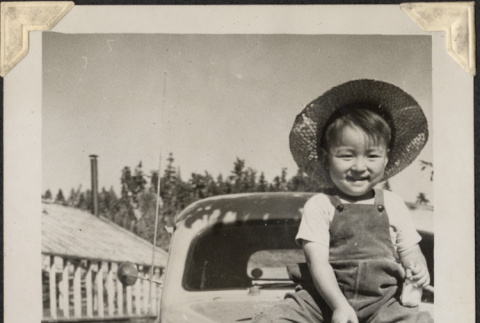 Boy in straw hat sitting on hood of car (ddr-densho-466-922)