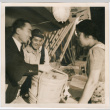 Two men handing a package wrapped in rope to woman across a table (ddr-densho-426-1871)