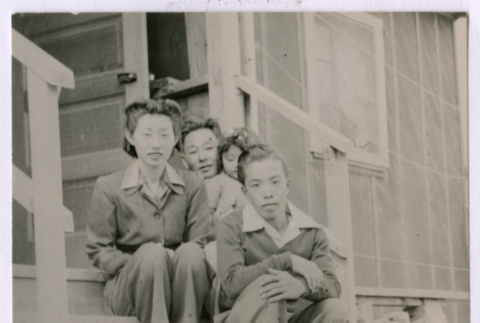 Japanese American woman and three children sit on barracks steps (ddr-densho-362-11)