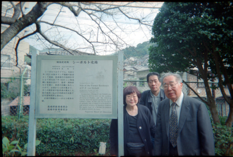 Tomoye, Norman and Henri Takahashi standing by sign for Siebold Residence, Nagasaki (ddr-densho-426-508)
