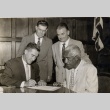 Neal Blaisdell signing a document while Duke Kahanamoku and two other men look on (ddr-njpa-2-497)