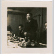 Man standing by table with food, two men seated on either side (ddr-densho-426-1933)