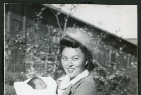 Photograph of a woman holding an infant in front of a building at Manzanar (ddr-csujad-47-234)