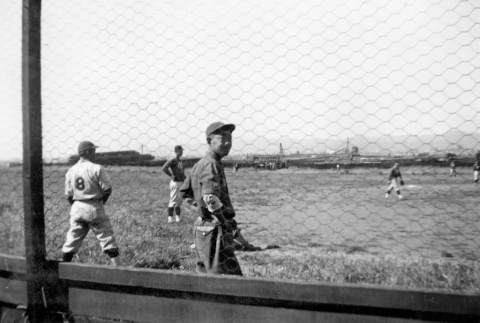 Men playing baseball in field, seen through fence (ddr-ajah-5-94)