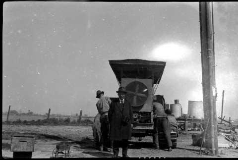 Man stands in front of workers and farming equipment (ddr-densho-480-64)