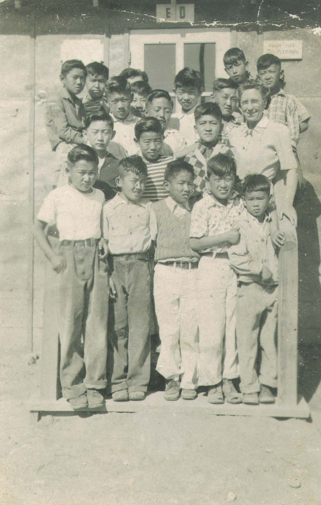 Group photo of Japanese American fifth graders standing on the steps in front of a barrack with their teacher in Minidoka.